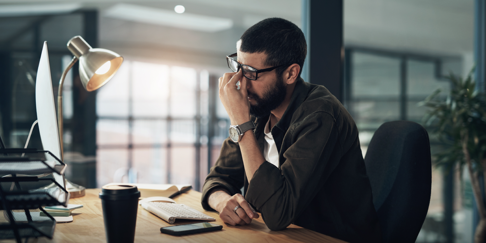 Stressed professional rubbing eyes at office desk with computer