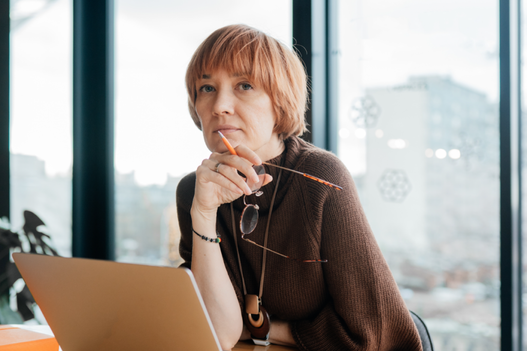 Thoughtful manager holding glasses while working at laptop by window