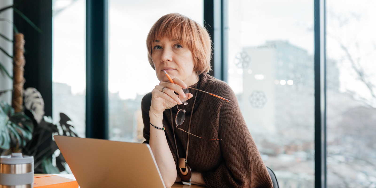 Thoughtful manager holding glasses while working at laptop by window